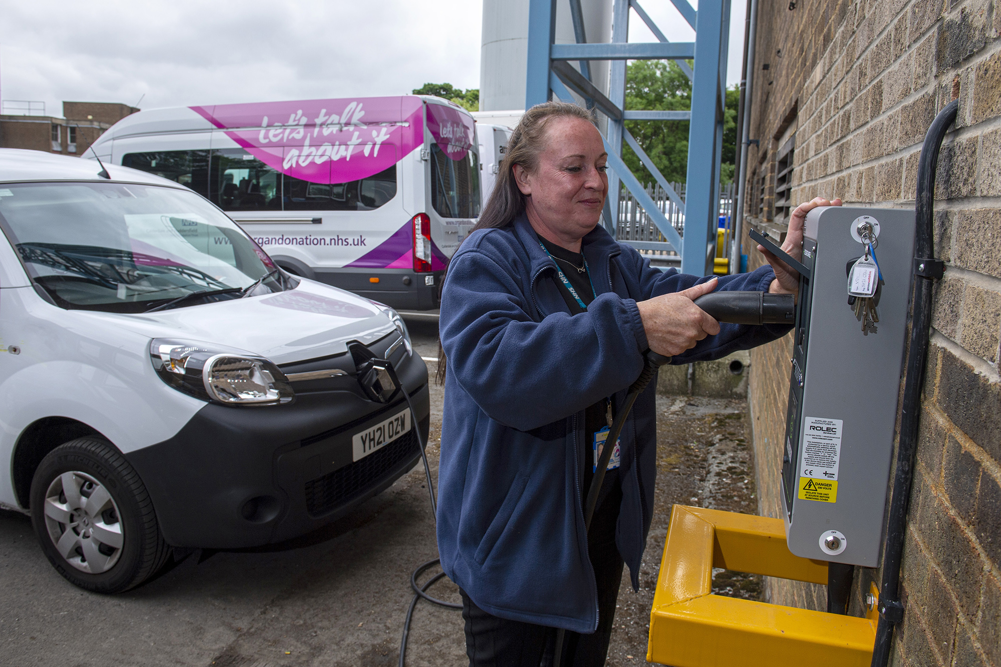 Female member of staff plugging in the electric car charging cable into the wall charger.