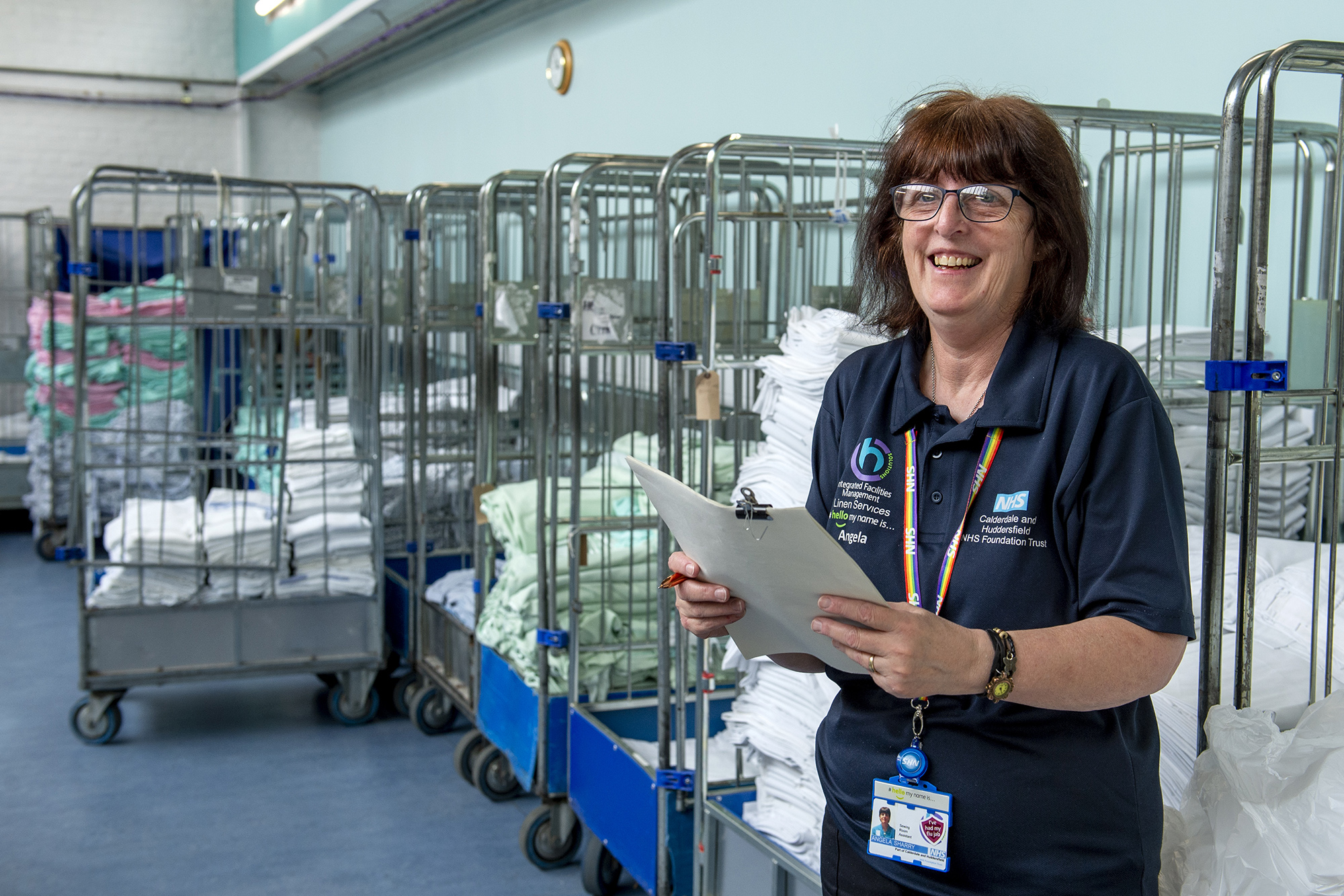 Female staff member smiling whilst holding paper with linen in crates behind her.