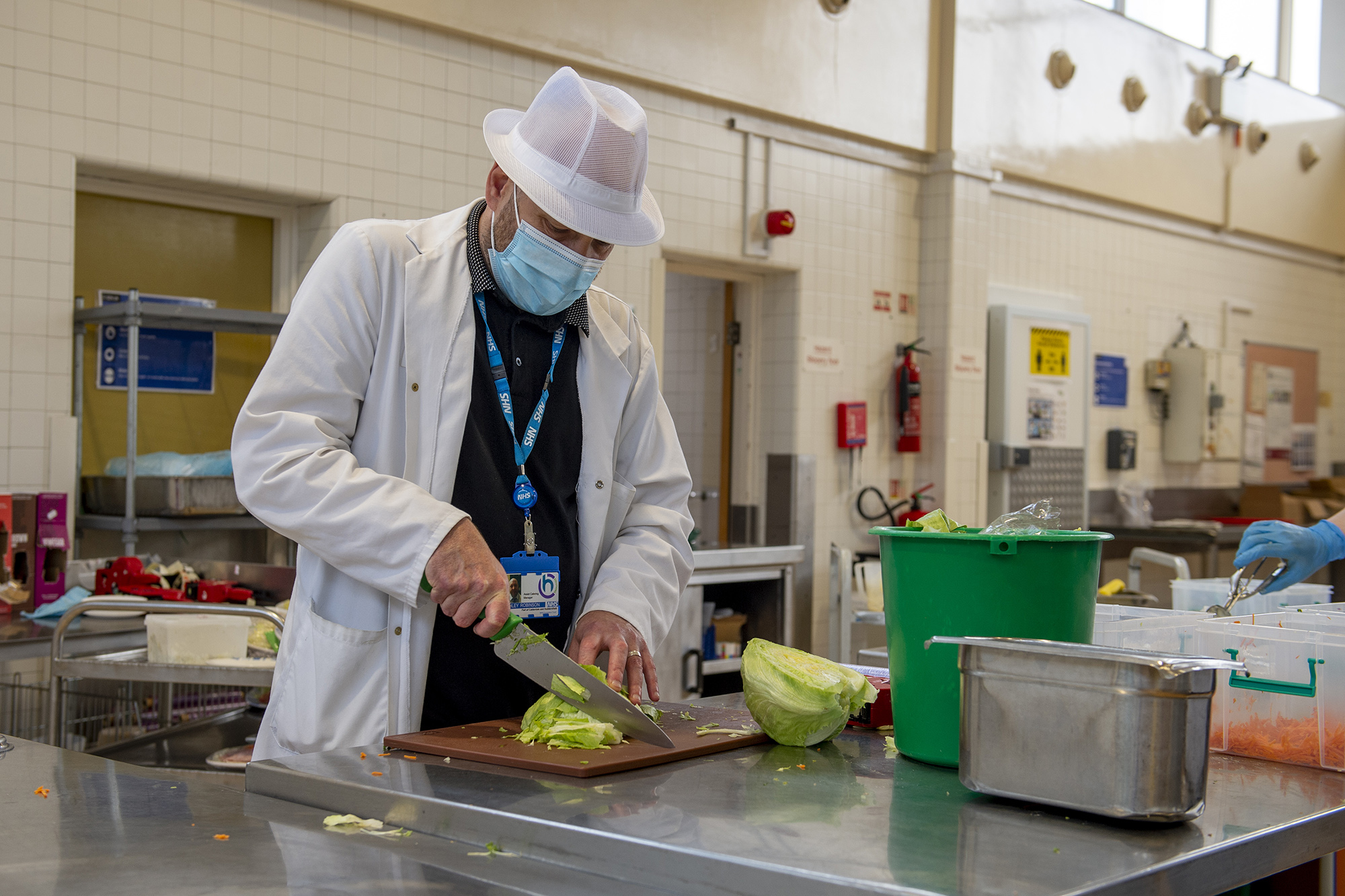 Male staff member preparing food in the kitchen wearing PPE.
